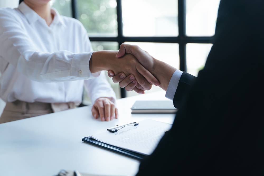 Two people shaking hands across a table in FL, with documents and a clipboard visible in the foreground, possibly sealing the deal with a notary near Kissimmee.