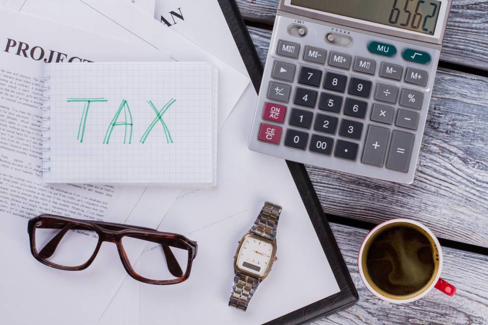 Notebook labeled "Tax," calculator, glasses, wristwatch, and coffee cup arranged on a wooden surface with documents, ready for review by a notary near Kissimmee.